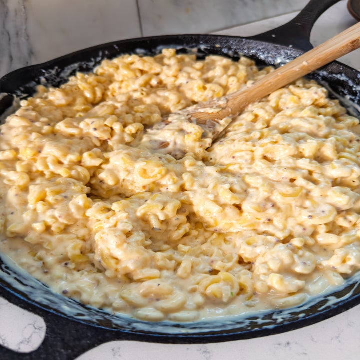 Creamy macaroni and cheese in a skillet with a wooden spoon stirring the noodles