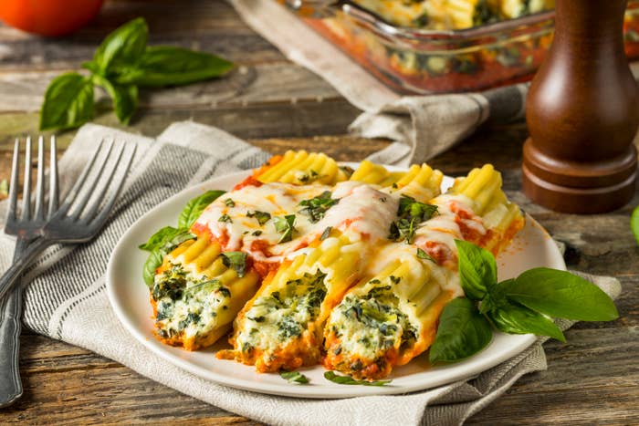 Plate of baked spinach-filled manicotti topped with melted cheese and herbs, garnished with fresh basil, on a rustic wooden table