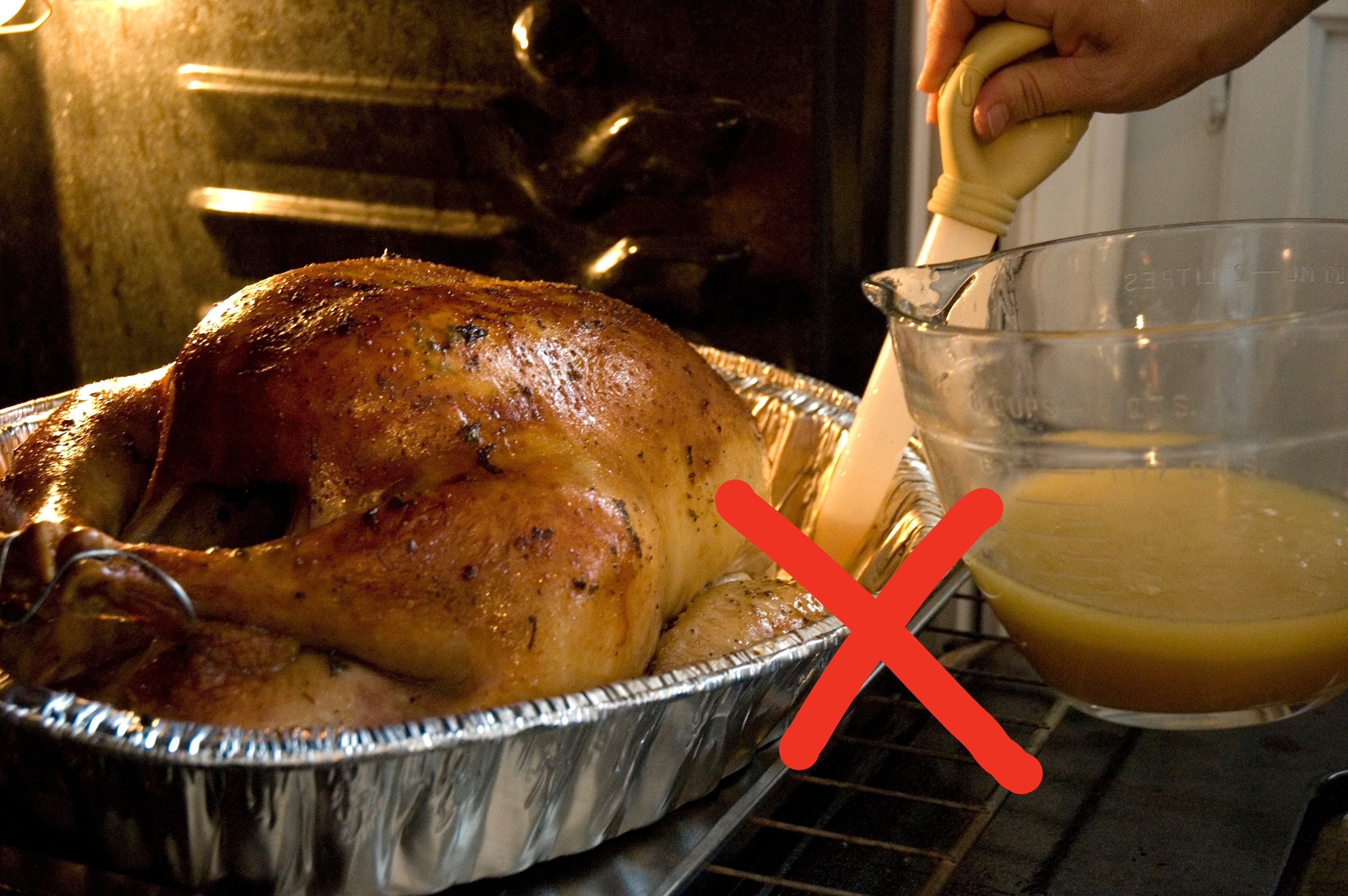 A whole roasted turkey in an oven is being basted with a spiced liquid from a glass bowl using a baster
