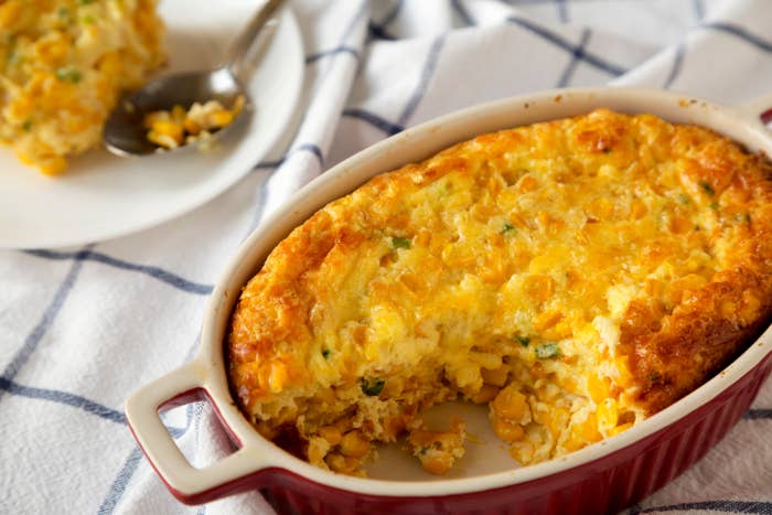 Baked corn casserole in a red dish with a serving spooned onto a plate, ready to eat