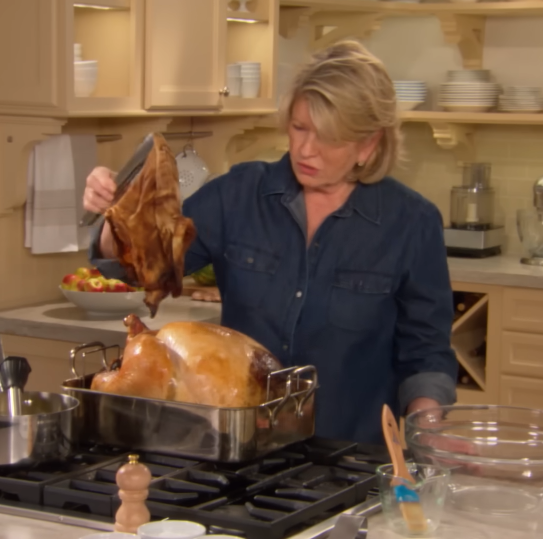 A person in a denim shirt prepares a roasted turkey in a kitchen setting