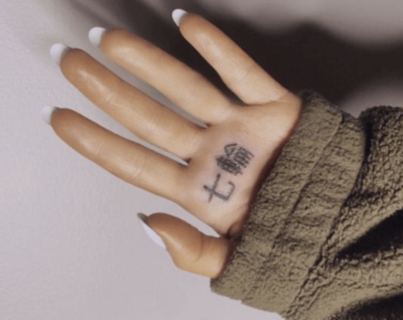A hand with well-groomed nails displays a tattoo of Asian characters on the palm, wearing a textured long-sleeve garment