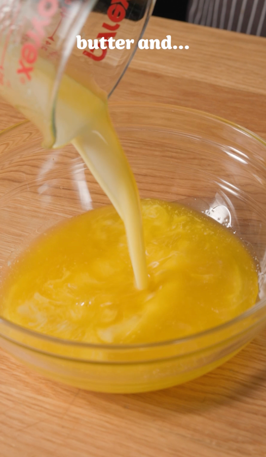 Butter being poured from a measuring cup into a glass bowl on a wooden surface