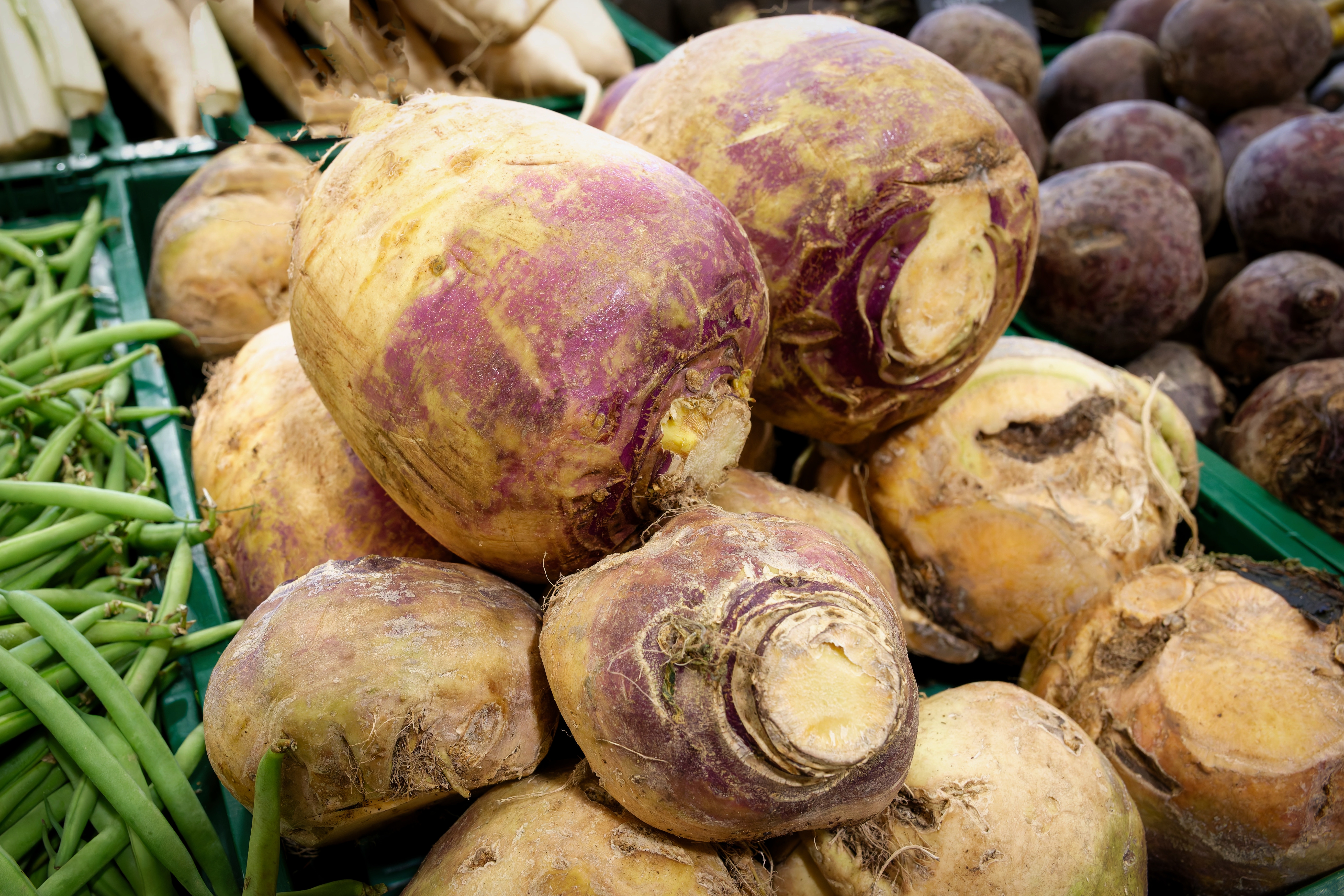 A pile of rutabagas on display at a market, surrounded by green beans and beets