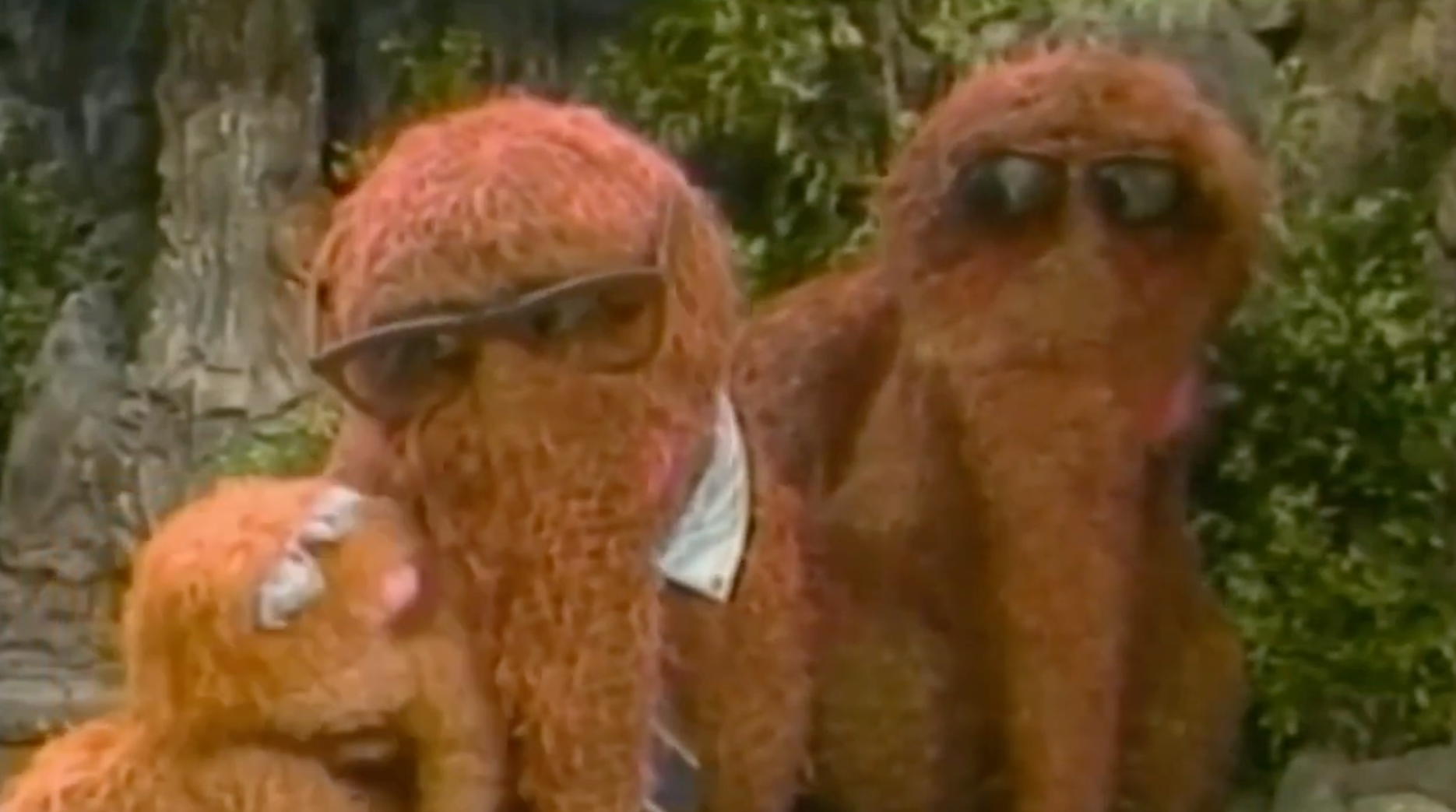 Three Muppet-like creatures with shaggy fur and sunglasses are gathered outdoors