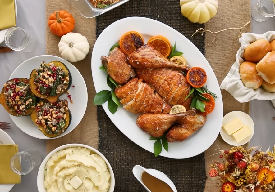 Thanksgiving spread with roasted turkey, mashed potatoes, stuffed squash, bread rolls, and festive pumpkins on a decorated table setting