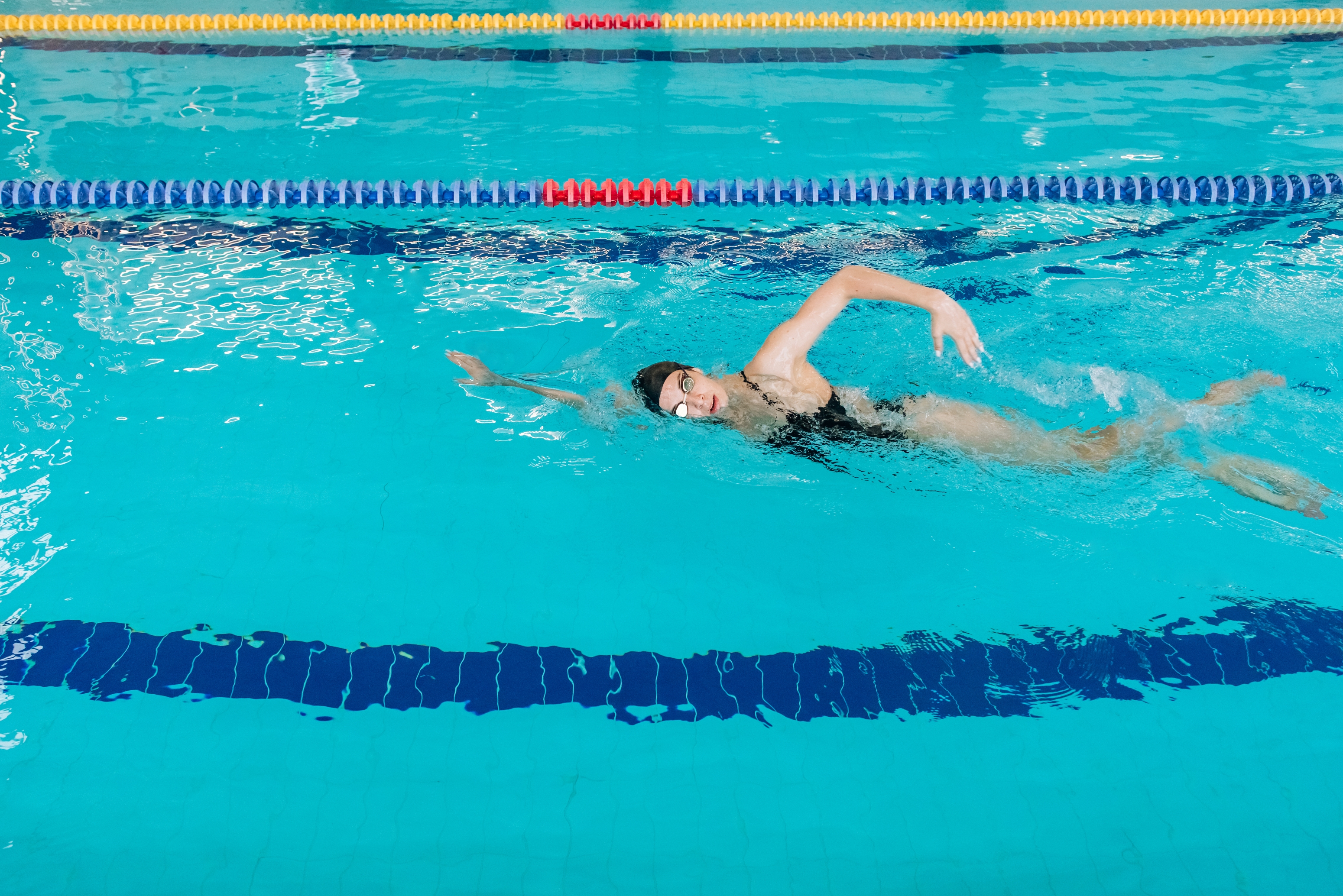 Person som svømmer freestyle i et basseng, har på seg badedrakt og briller, med fokus på å holde seg strømlinjeformet og effektiv i vannet