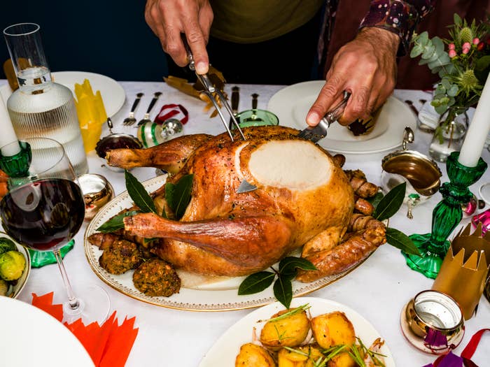 A person carves a roasted turkey on a festive table with side dishes, wine, and elegant tableware, creating a celebratory dining atmosphere