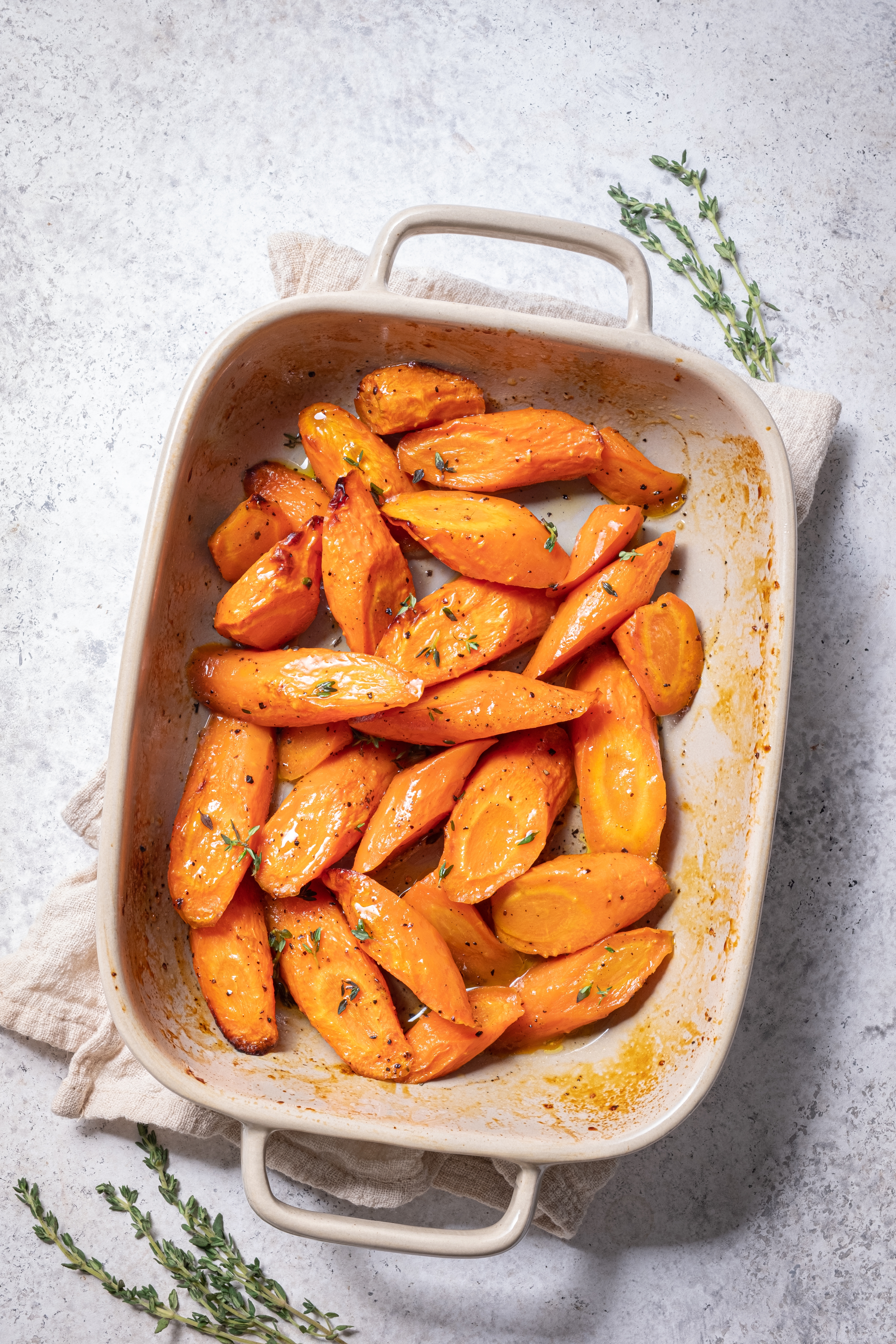 Roasted sweet potato wedges in a baking dish, garnished with fresh herbs, displayed on a light surface with sprigs of thyme nearby