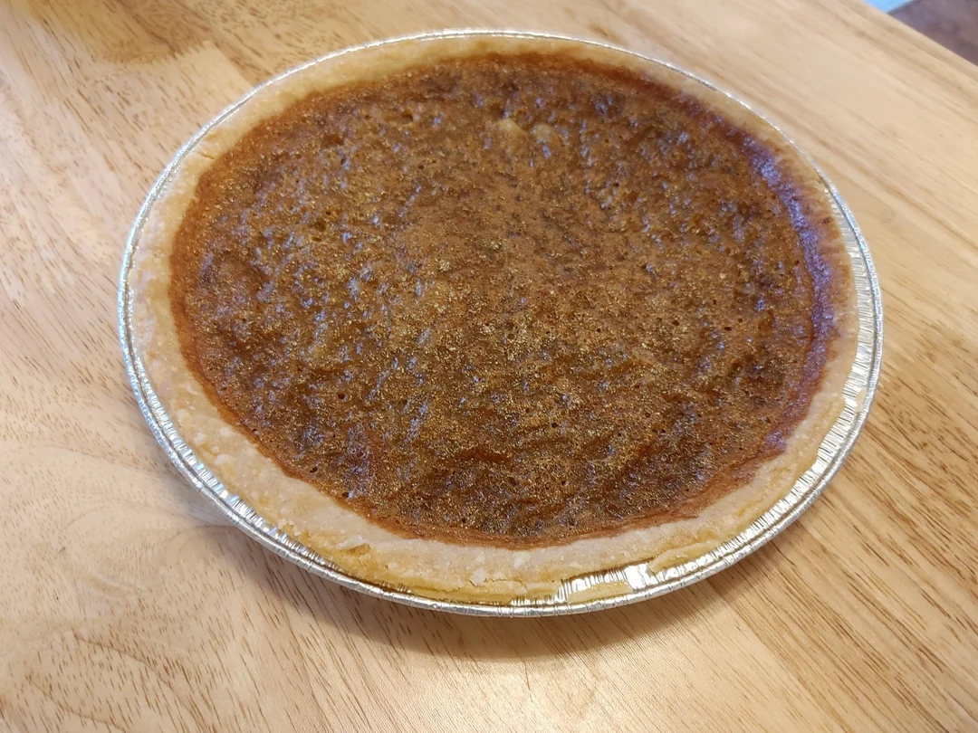 A baked pie with a golden, flaky crust and a smooth filling sits on a wooden table, representing a classic dessert option