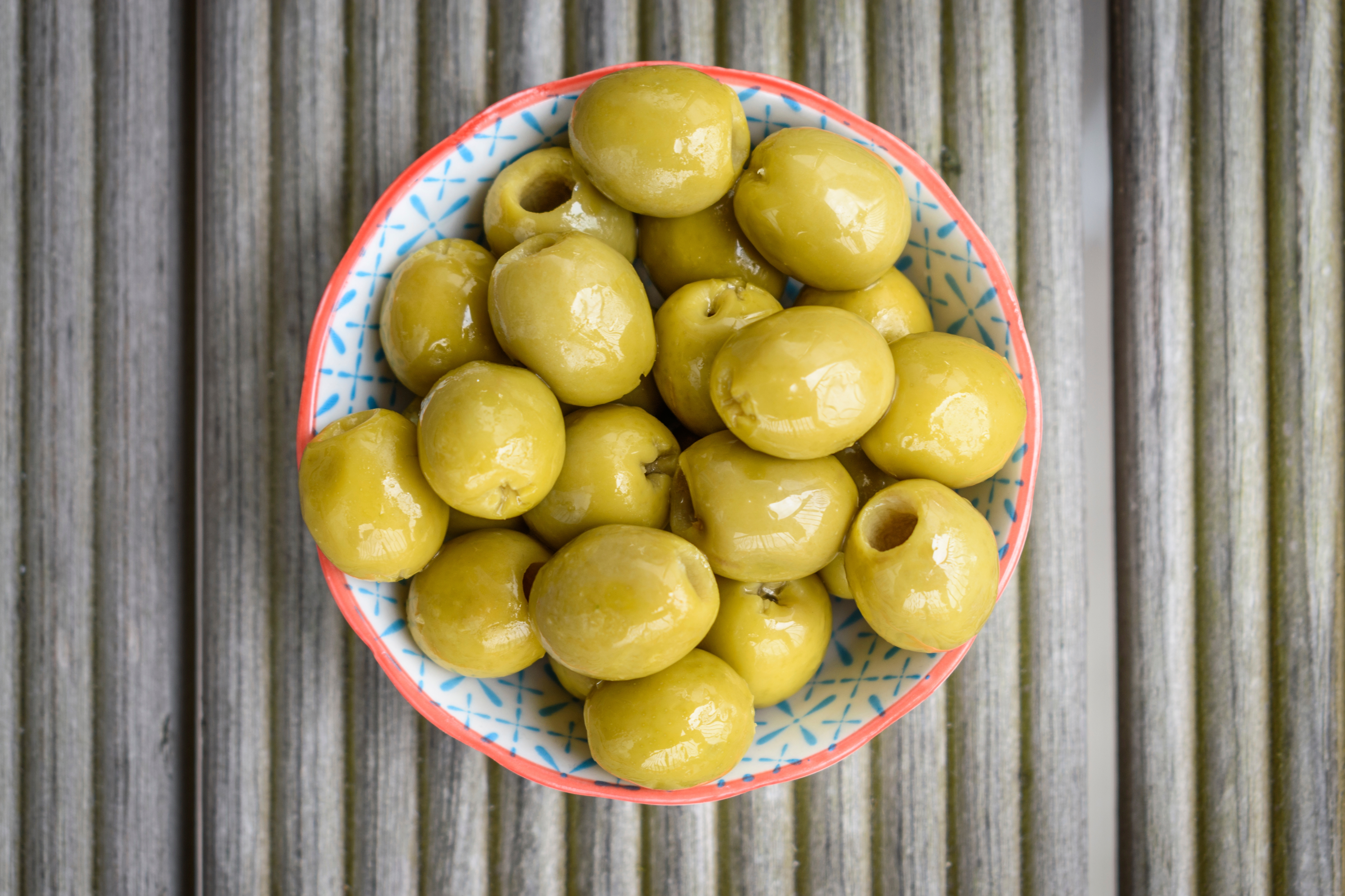 A bowl of green olives on a textured wooden surface