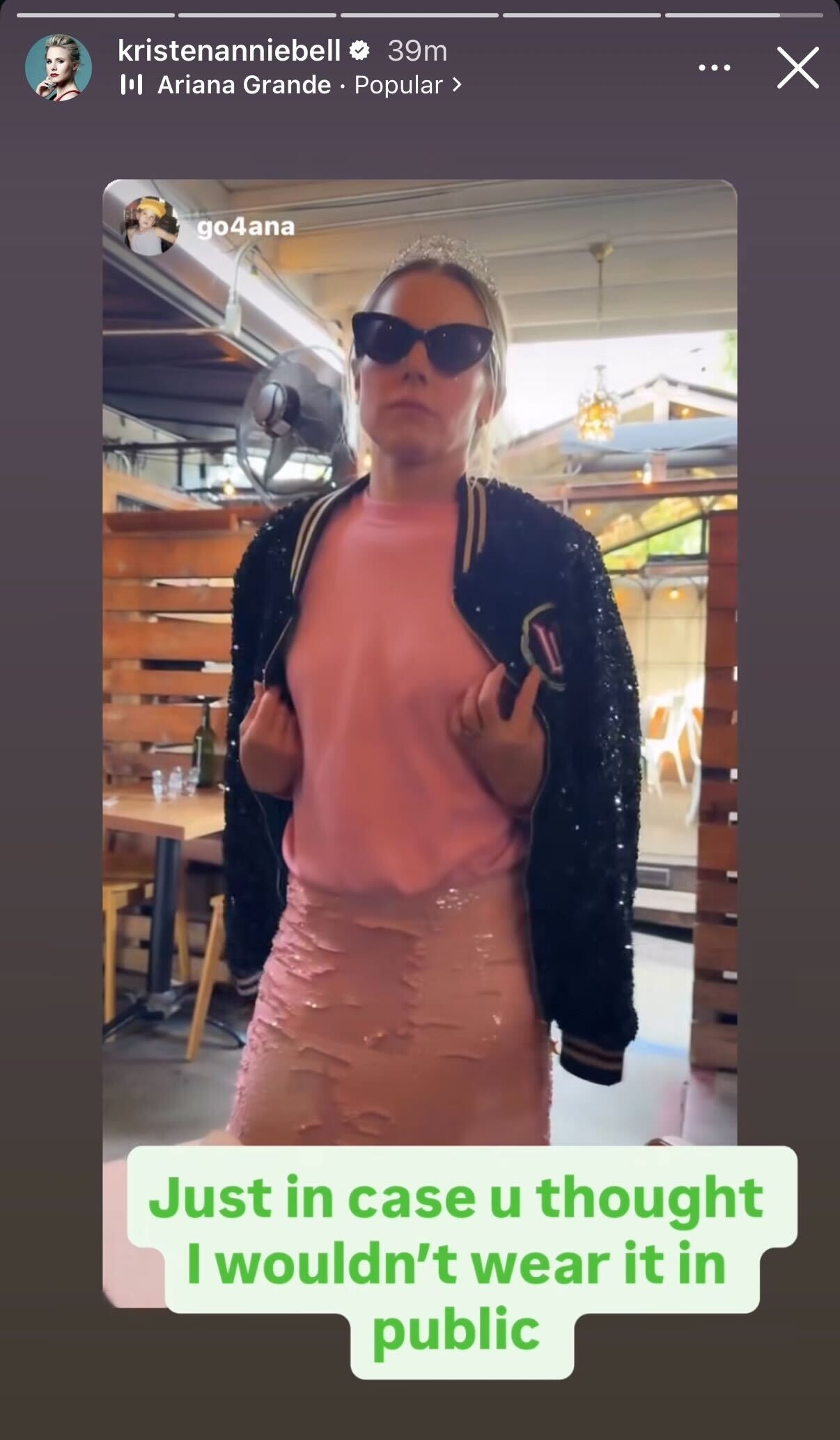 Kristen Bell wearing a casual chic outfit with a sequined pencil skirt, letterman jacket, and sunglasses, standing in a stylish indoor setting