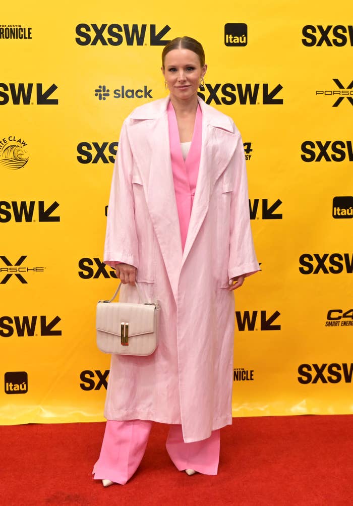 Kristen Bell in a suit and long coat on a red carpet at SXSW holding a purse