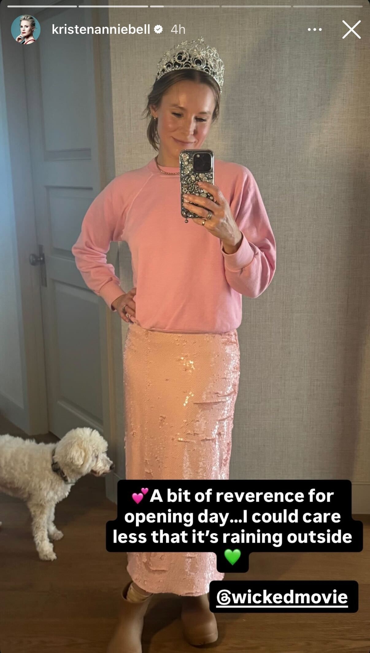 Kristen Bell wearing a crown, sweatshirt, and sequin skirt takes a mirror selfie