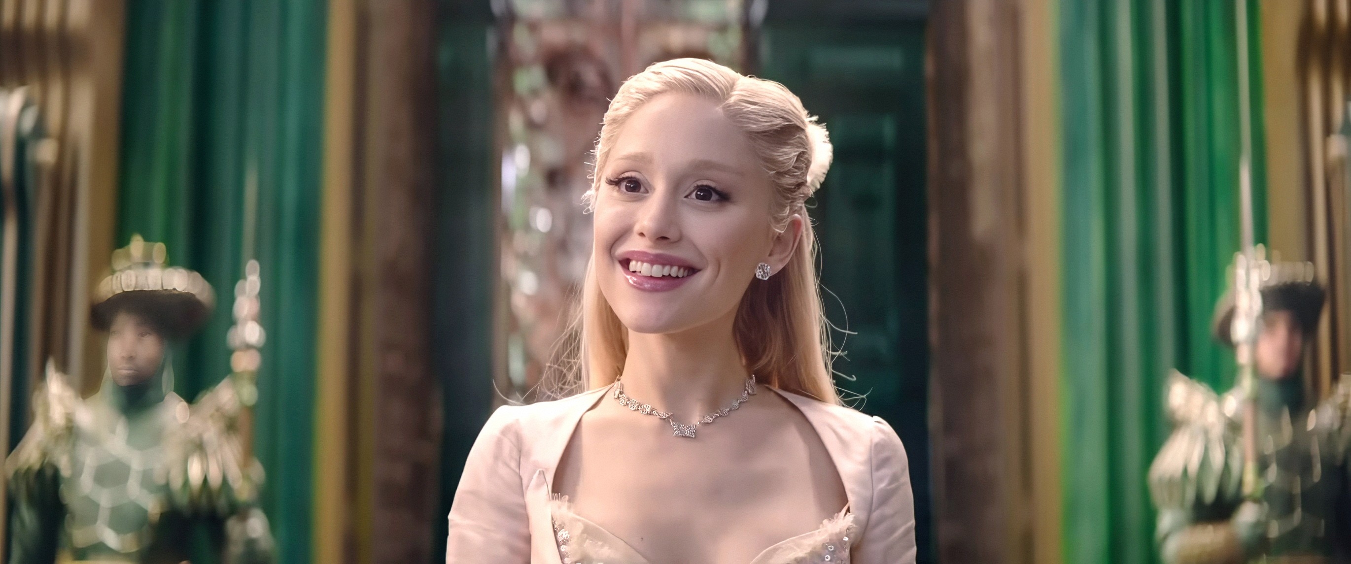 Ariana Grande in elegant, vintage-style dress and necklace, smiling in an ornate room with green accents in the background