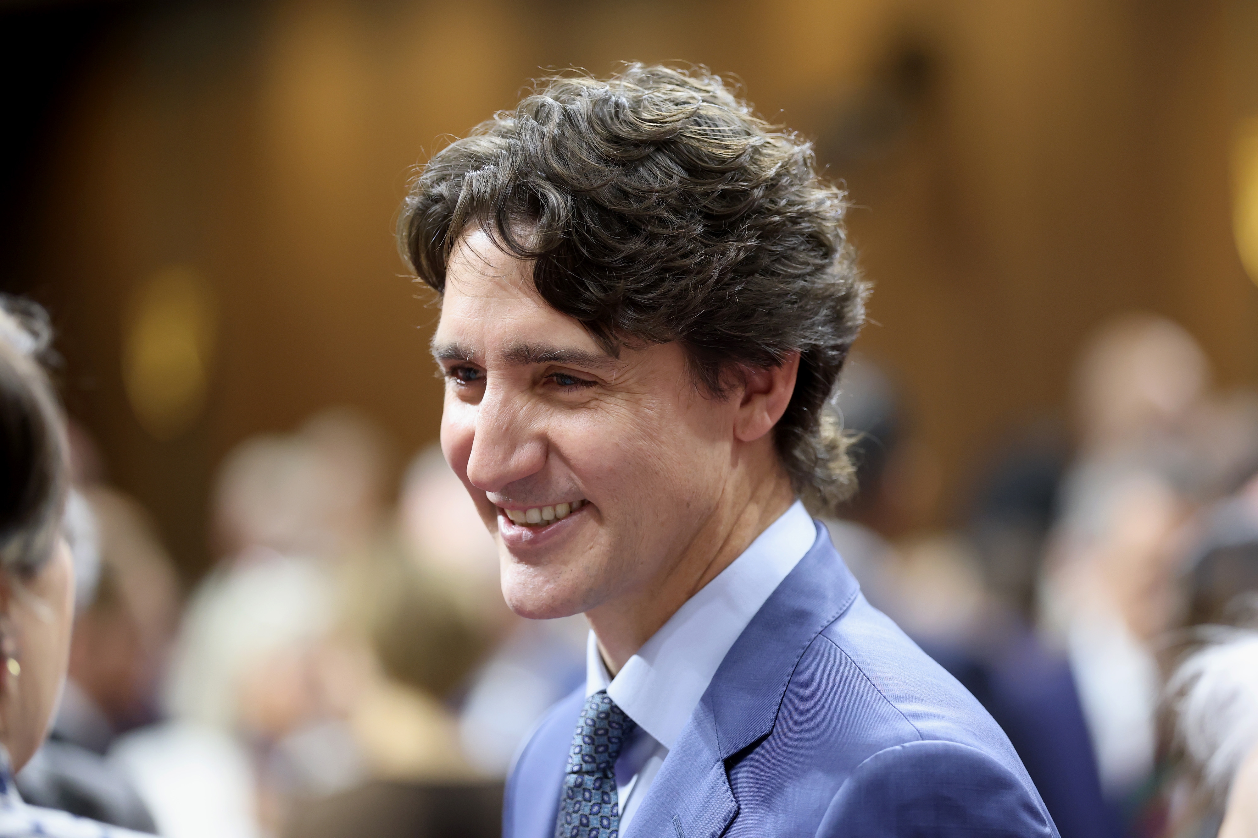Justin Trudeau in a suit at a formal event, conversing with others in a busy venue