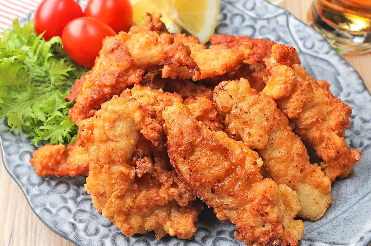 お皿に盛られた揚げた鶏肉、添えられたレモン、ミニトマト、葉野菜が飾られている。