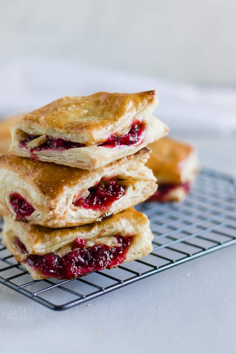 Three flaky pastries with a fruit filling, stacked on a cooling rack