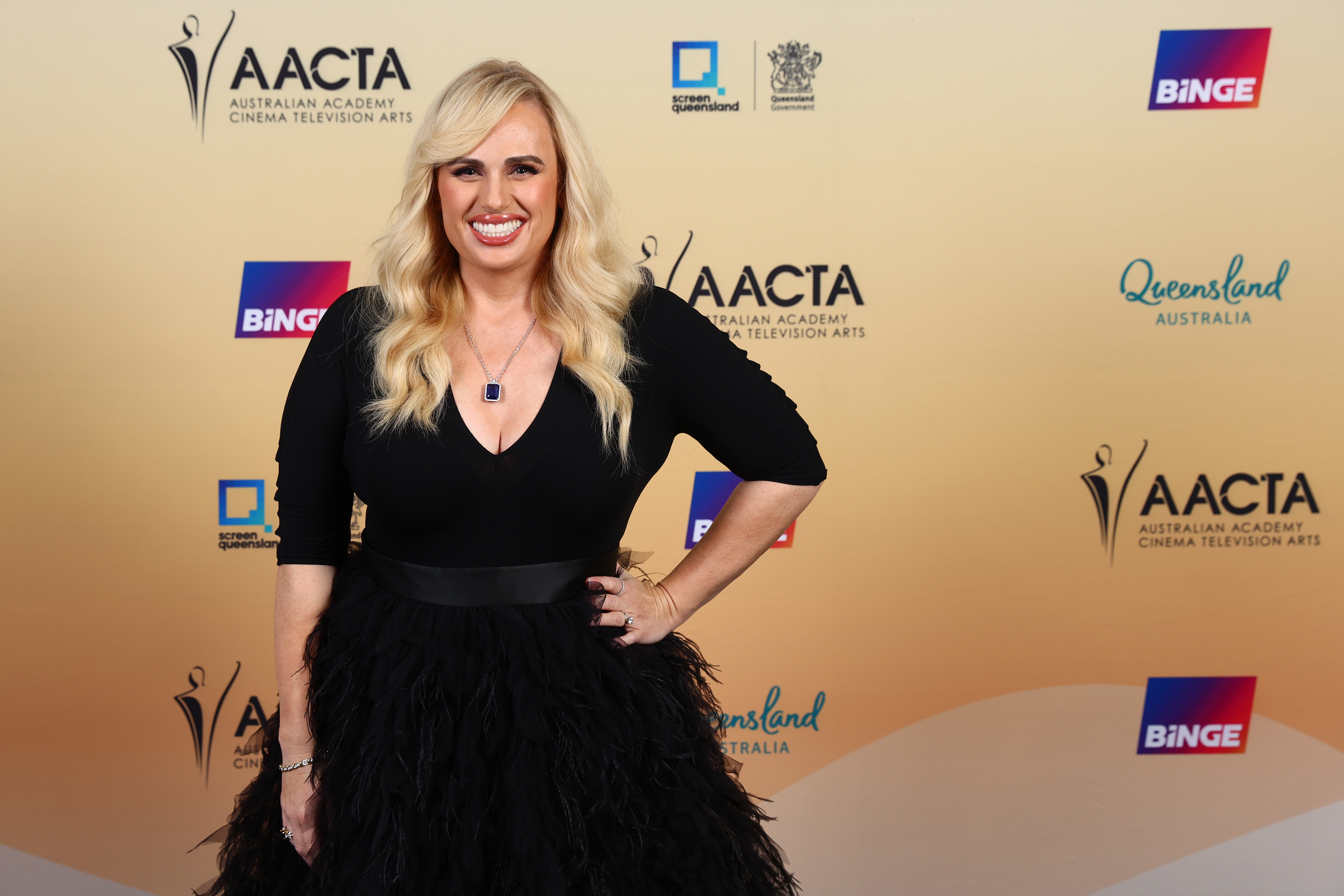Rebel Wilson in a black feathered gown on a red carpet at the AACTA Awards