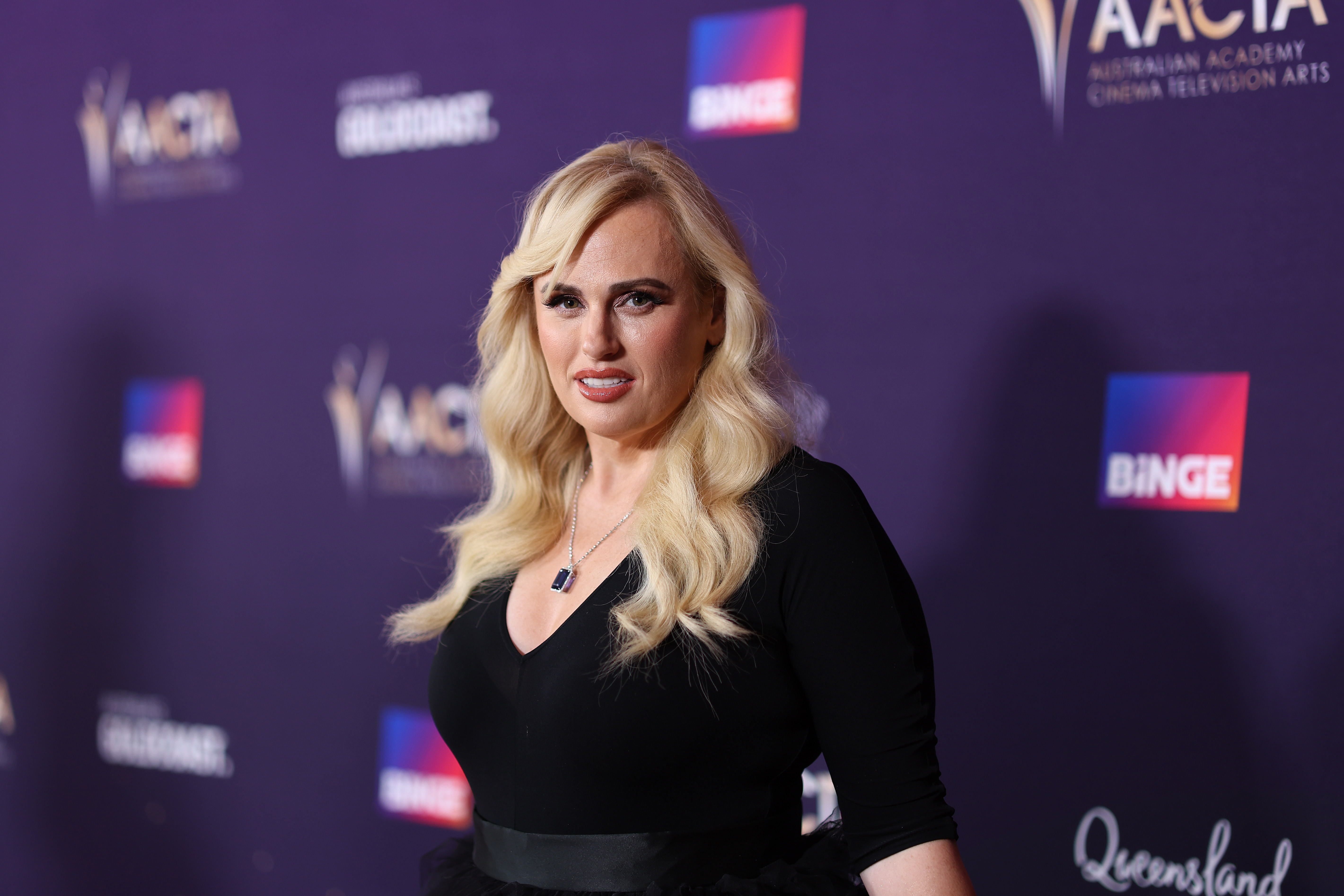 Rebel Wilson on the AACTA red carpet wears a black outfit with a V-neckline and has long wavy hair