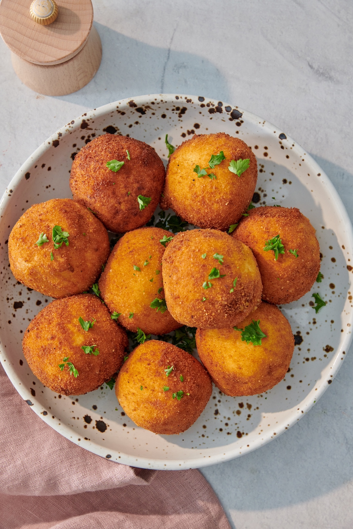 A plate of crispy fried arancini garnished with herbs, placed on a speckled dish