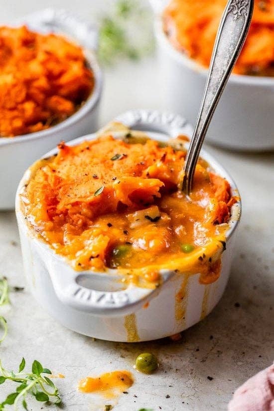 A mini casserole dish filled with a cheesy, baked vegetable dish with a spoon, topped with herbs and mashed potatoes