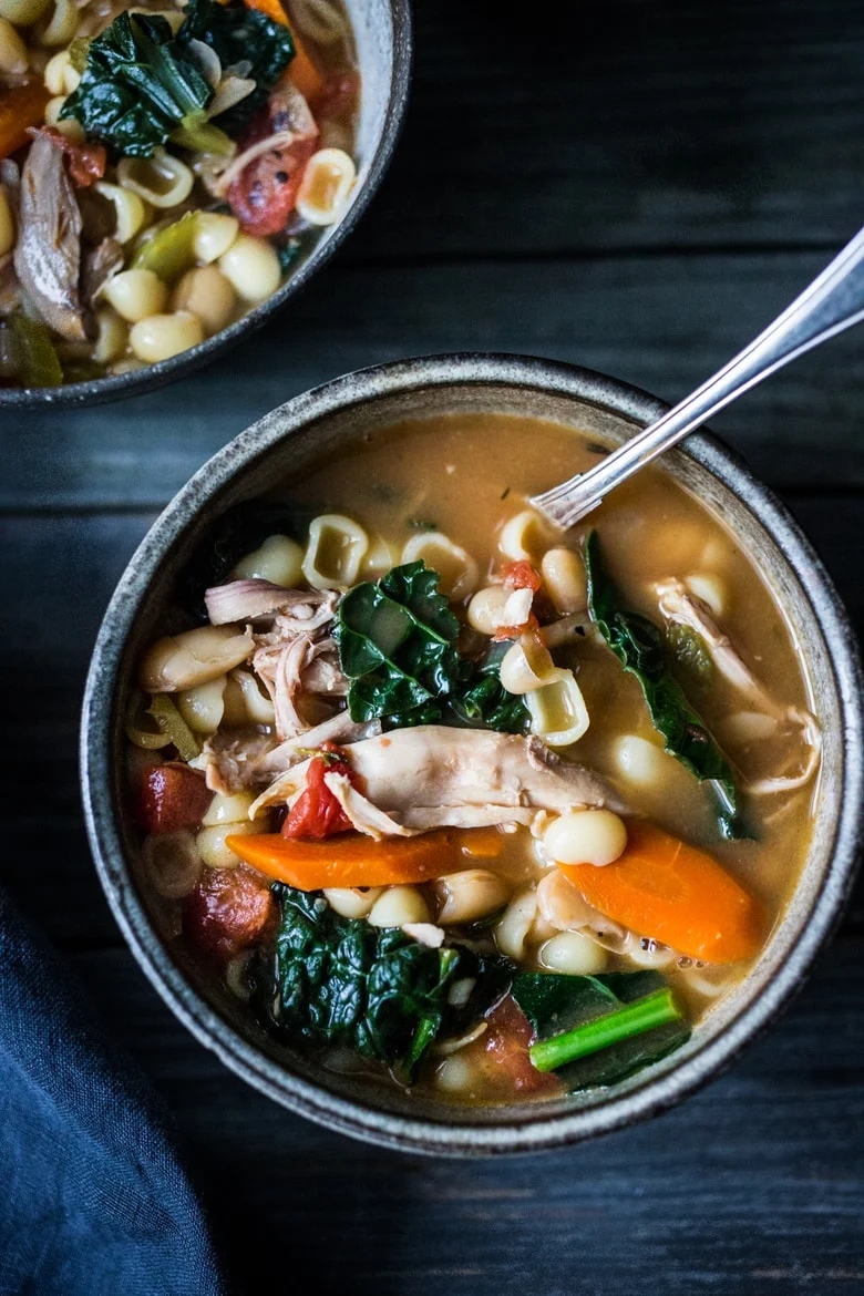 Bowl of hearty vegetable soup with chicken, carrots, and greens, featuring a spoon ready for eating