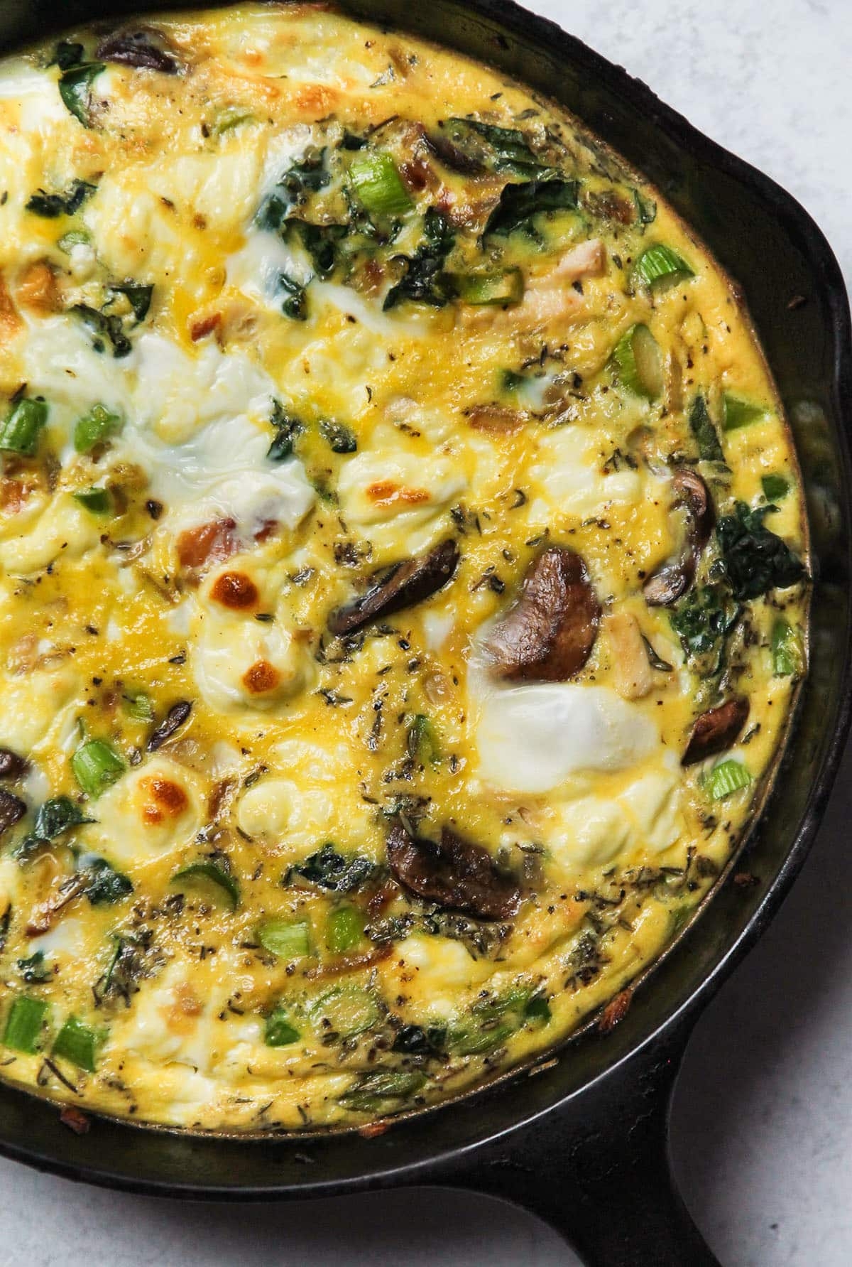 Frittata in a skillet with mushrooms, spinach, and cheese