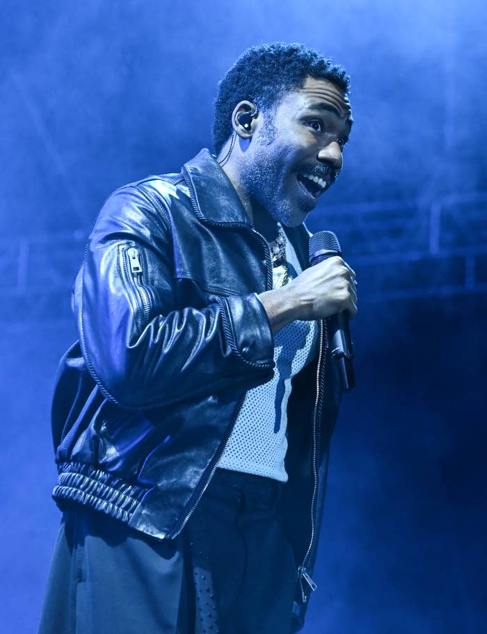 Donald Glover sings energetically on stage, wearing a stylish leather jacket over a mesh top
