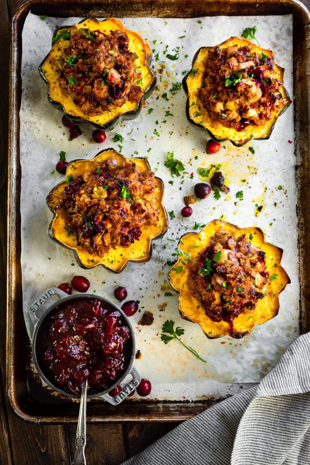 Roasted acorn squash halves filled with a savory stuffing, garnished with cranberries and herbs, beside a small pot of cranberry sauce