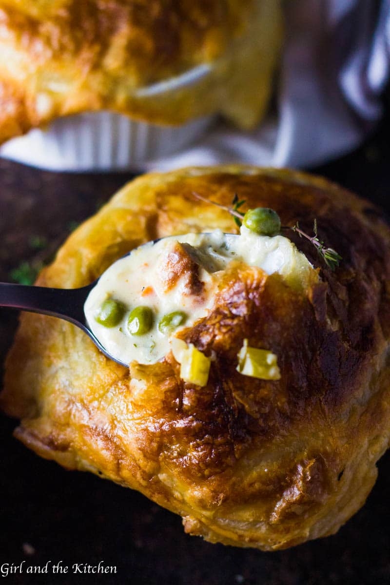 A spoon holds creamy chicken pot pie filling with peas, resting on a flaky pastry crust