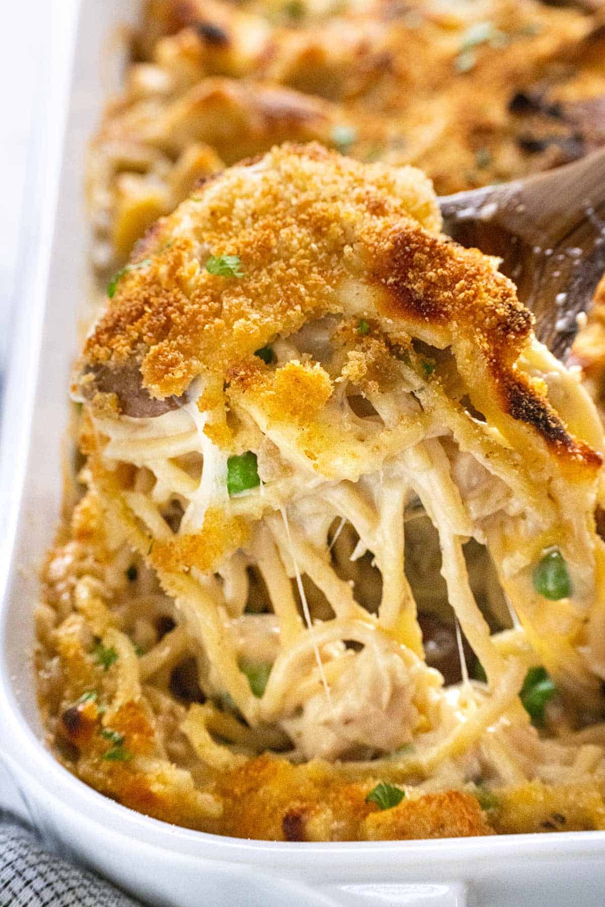 Cheesy casserole with pasta, peas, and breadcrumb topping being served from a dish, showcasing gooey texture