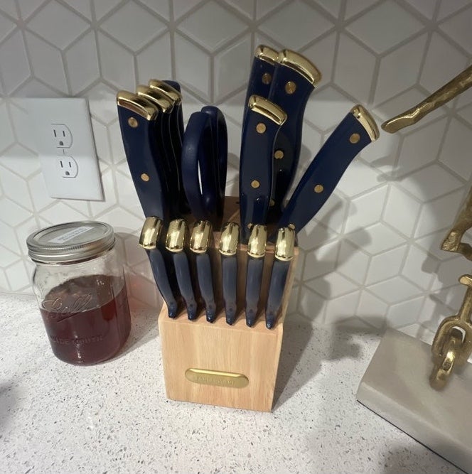 Knife set with dark handles and gold accents in a wooden block on a kitchen counter