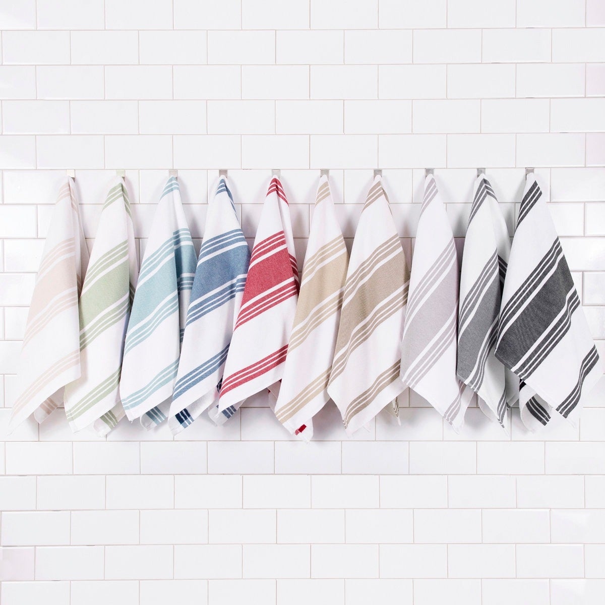 Nine striped towels hanging on hooks against a white tile background