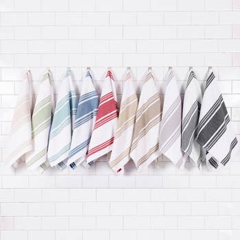 Nine striped towels hanging on hooks against a white tile background