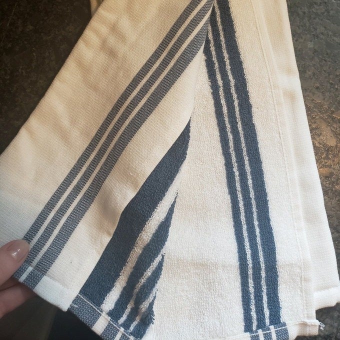 White kitchen towel with navy blue stripes, held by a hand, placed on a countertop. Ideal for everyday kitchen use