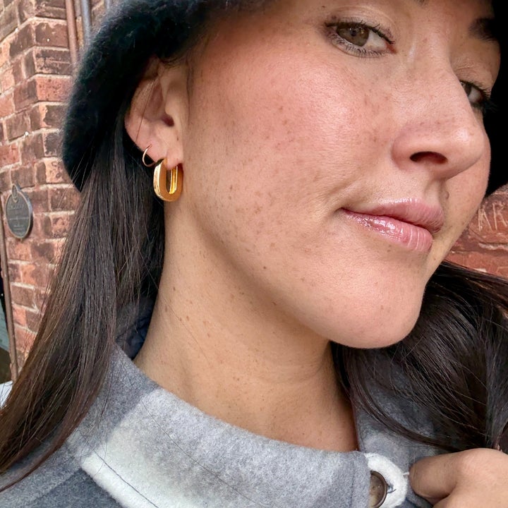 A person wearing a felt hat and statement hoop earrings, close-up shot focuses on accessories