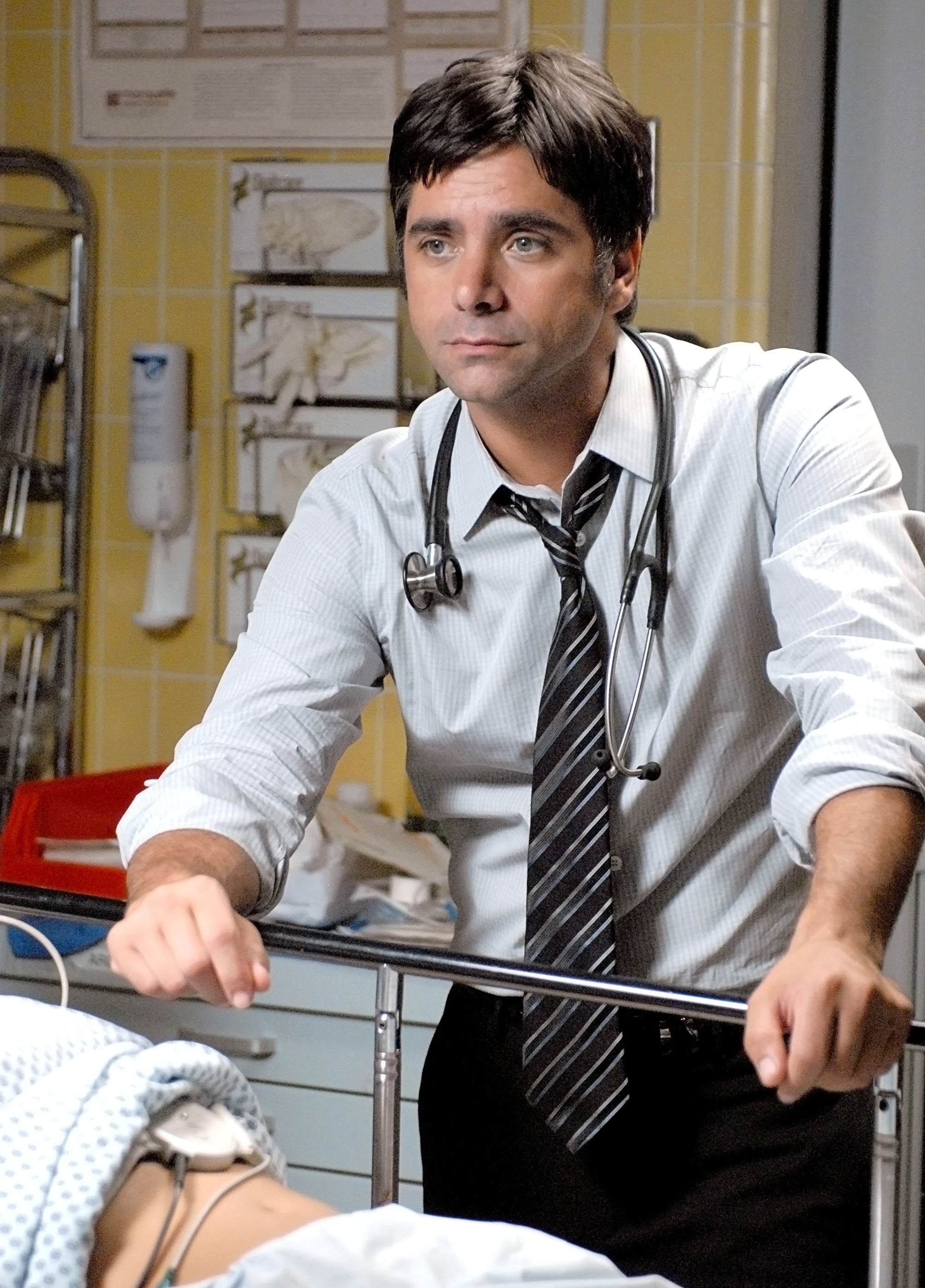 A man wearing a tie and button-up shirt, looking over a medical patient