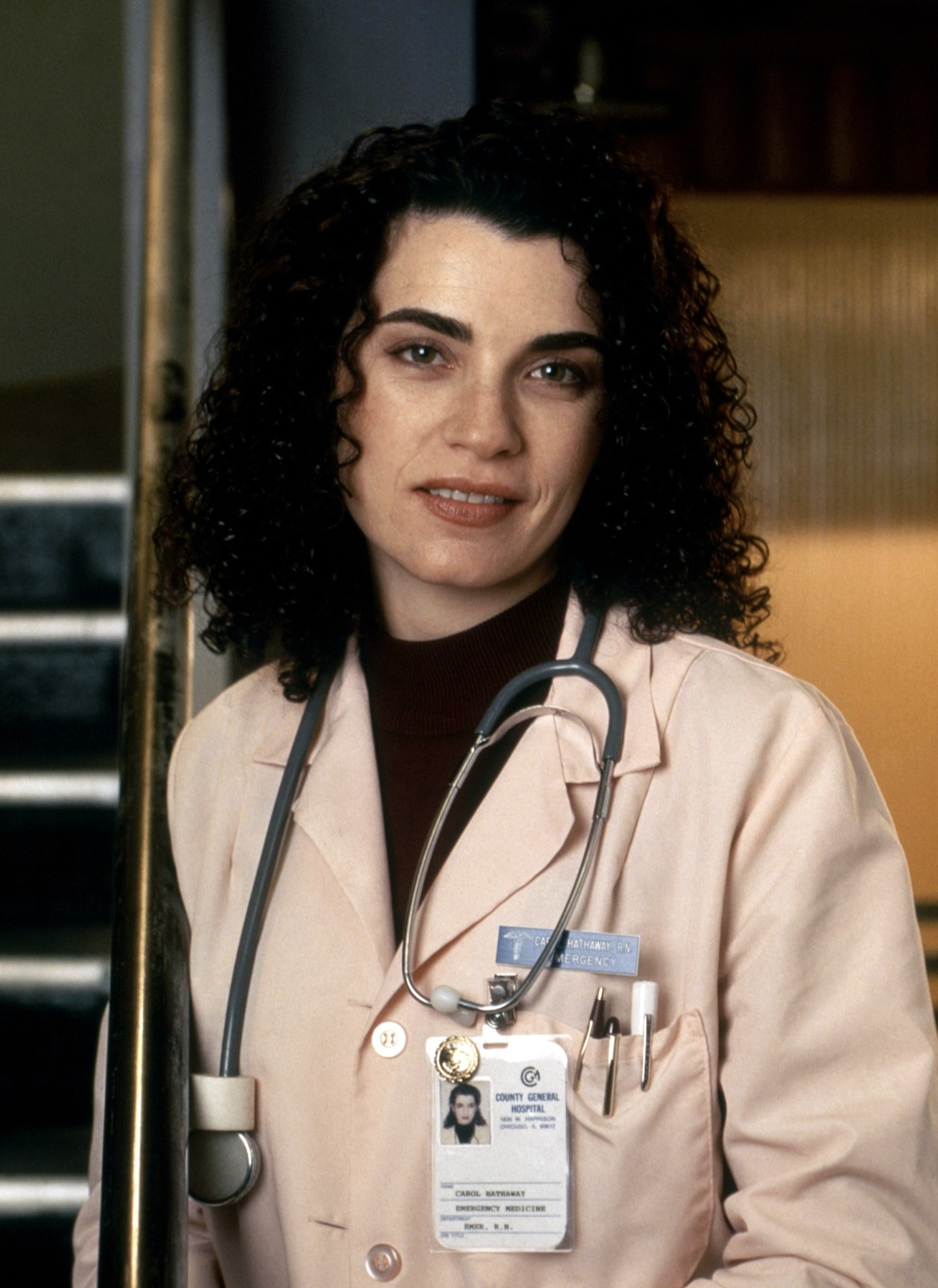A woman wearing a pink lab coat and an ID badge with medical accessories around her neck