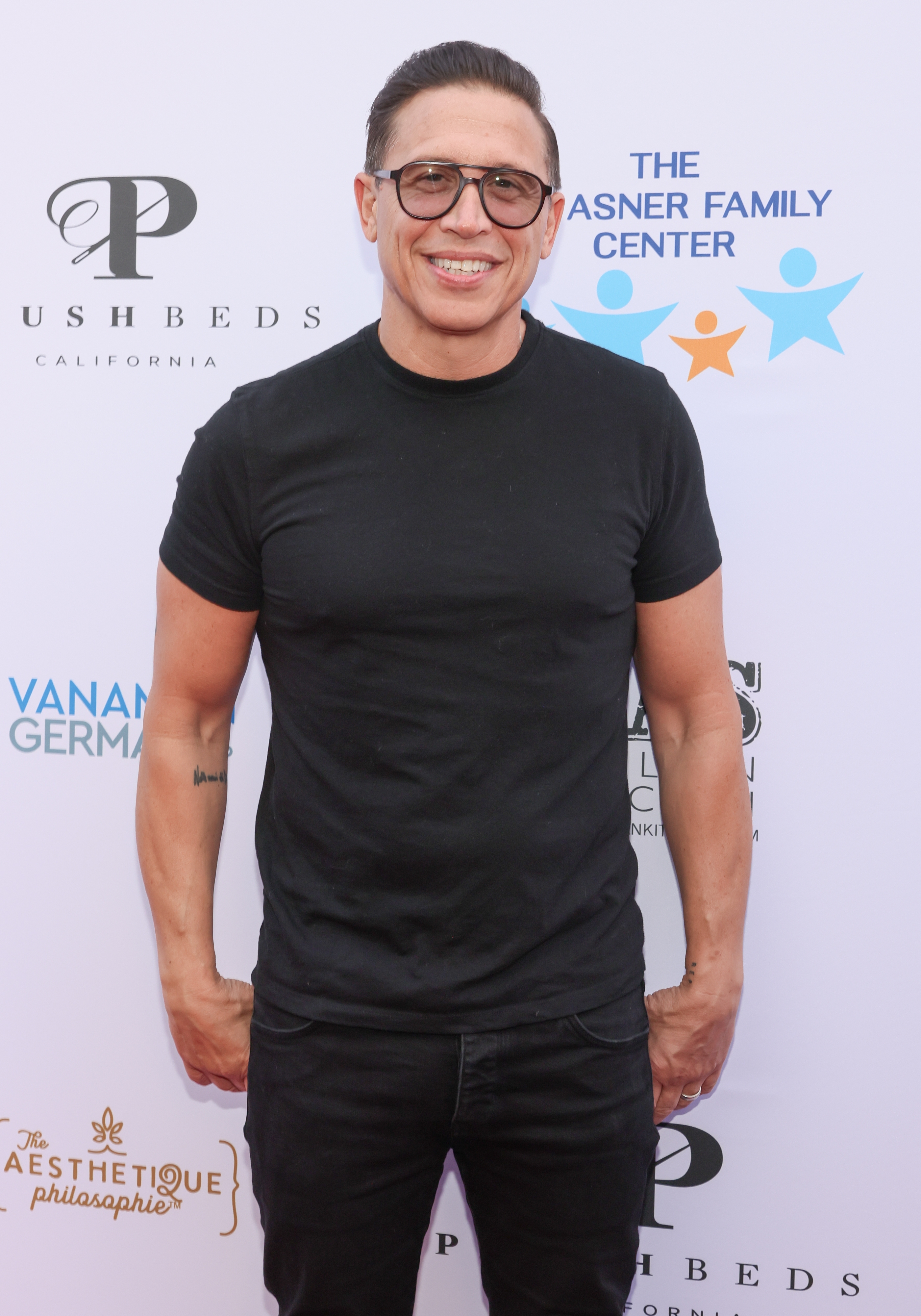 A person in a black t-shirt and glasses at a charity event backdrop