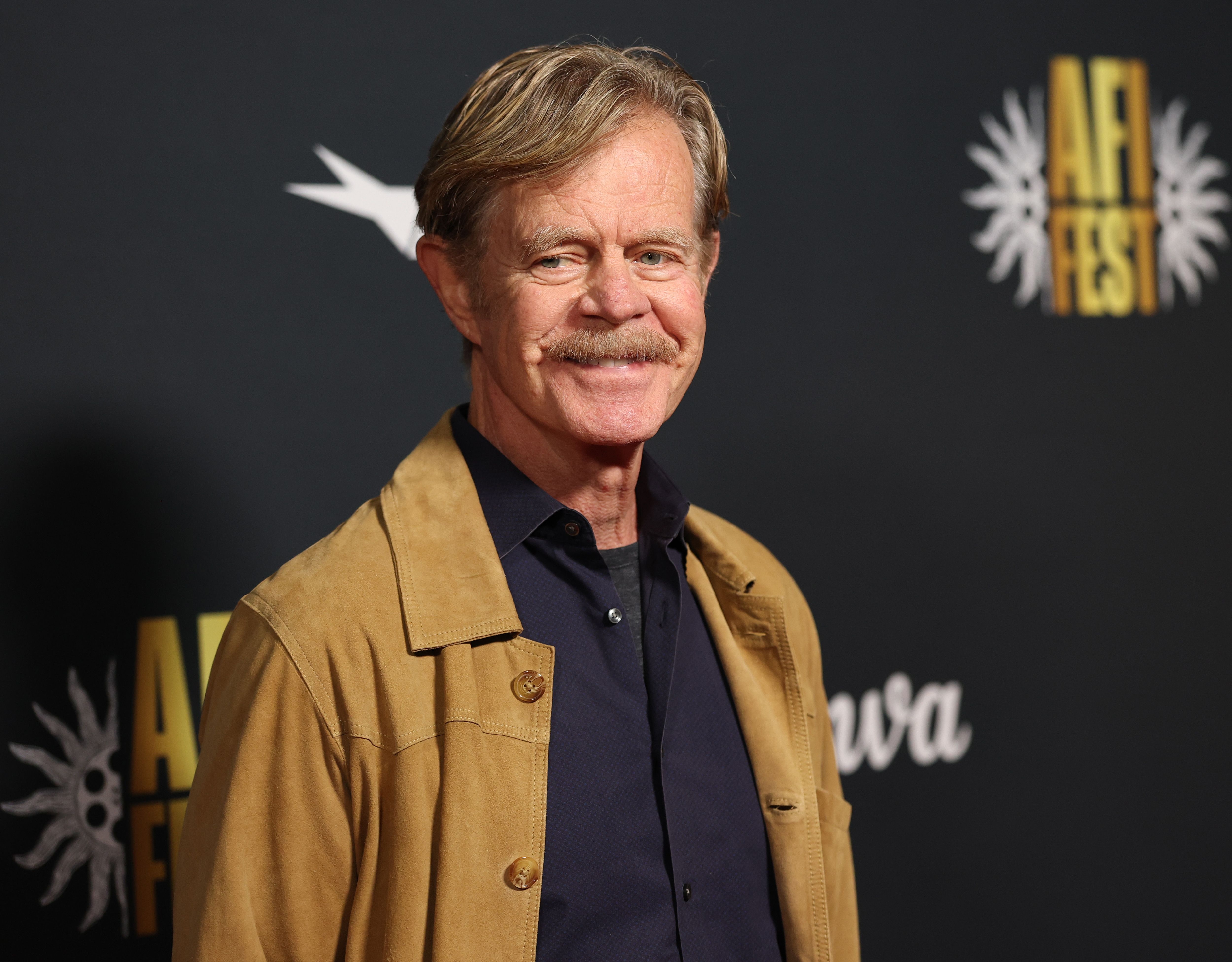 A man wearing a casual brown jacket and black button-up shirt