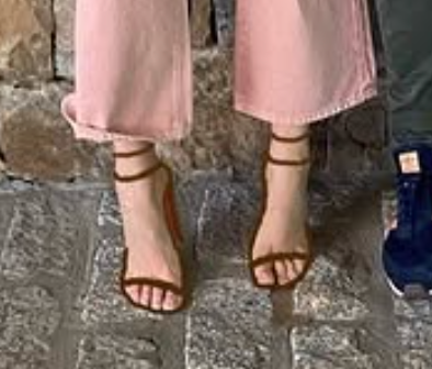 Person wearing strappy sandals with wide-legged pants standing on a stone pavement