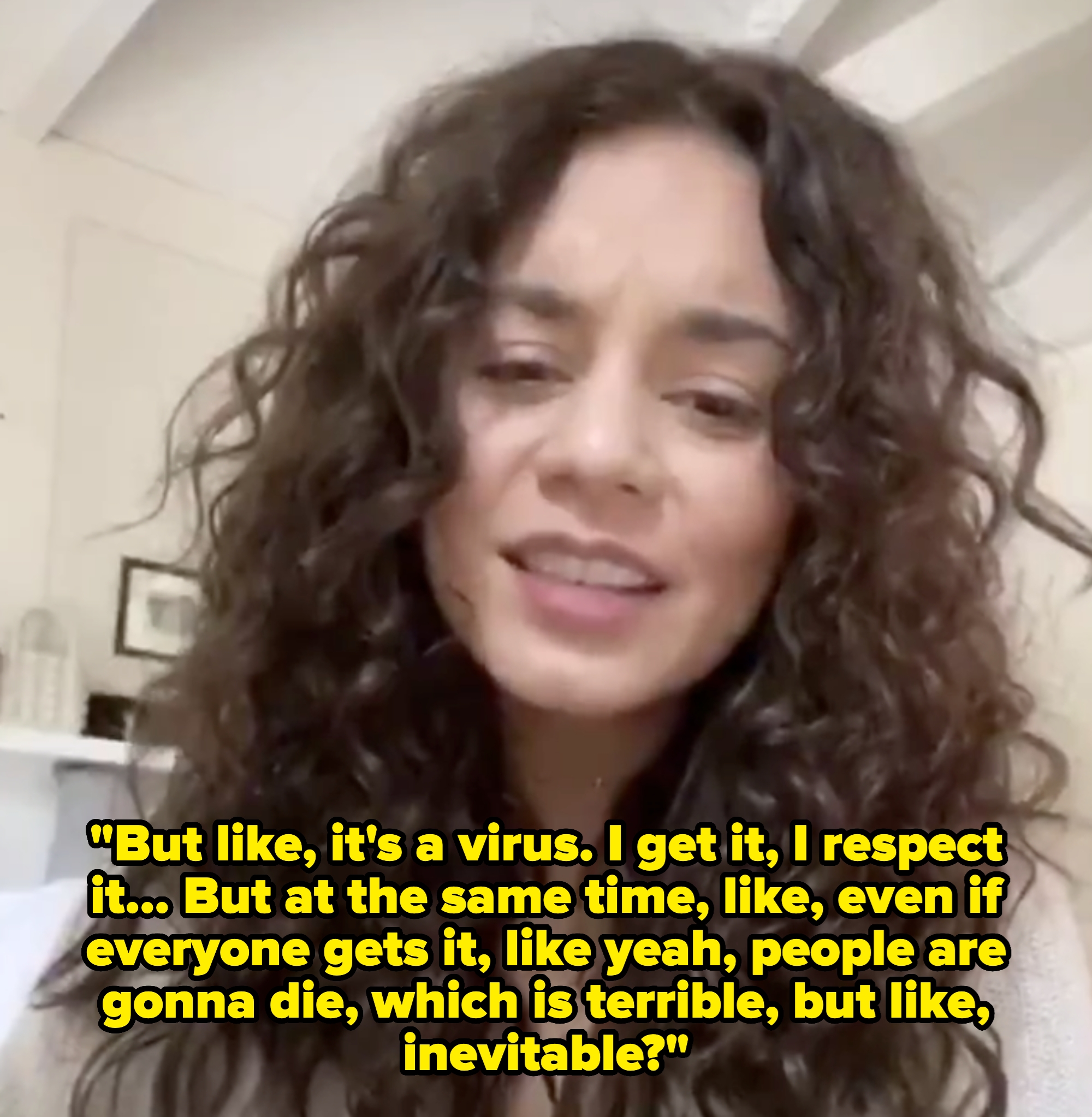 A person with curly hair smiling indoors, wearing a casual top