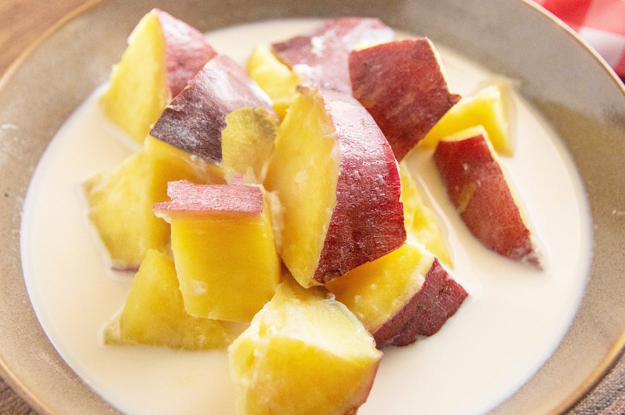 クリーミーなミルクソースに包まれたさつまいもの角切りがボウルに盛られています。背景にチェック柄の布が見えます。