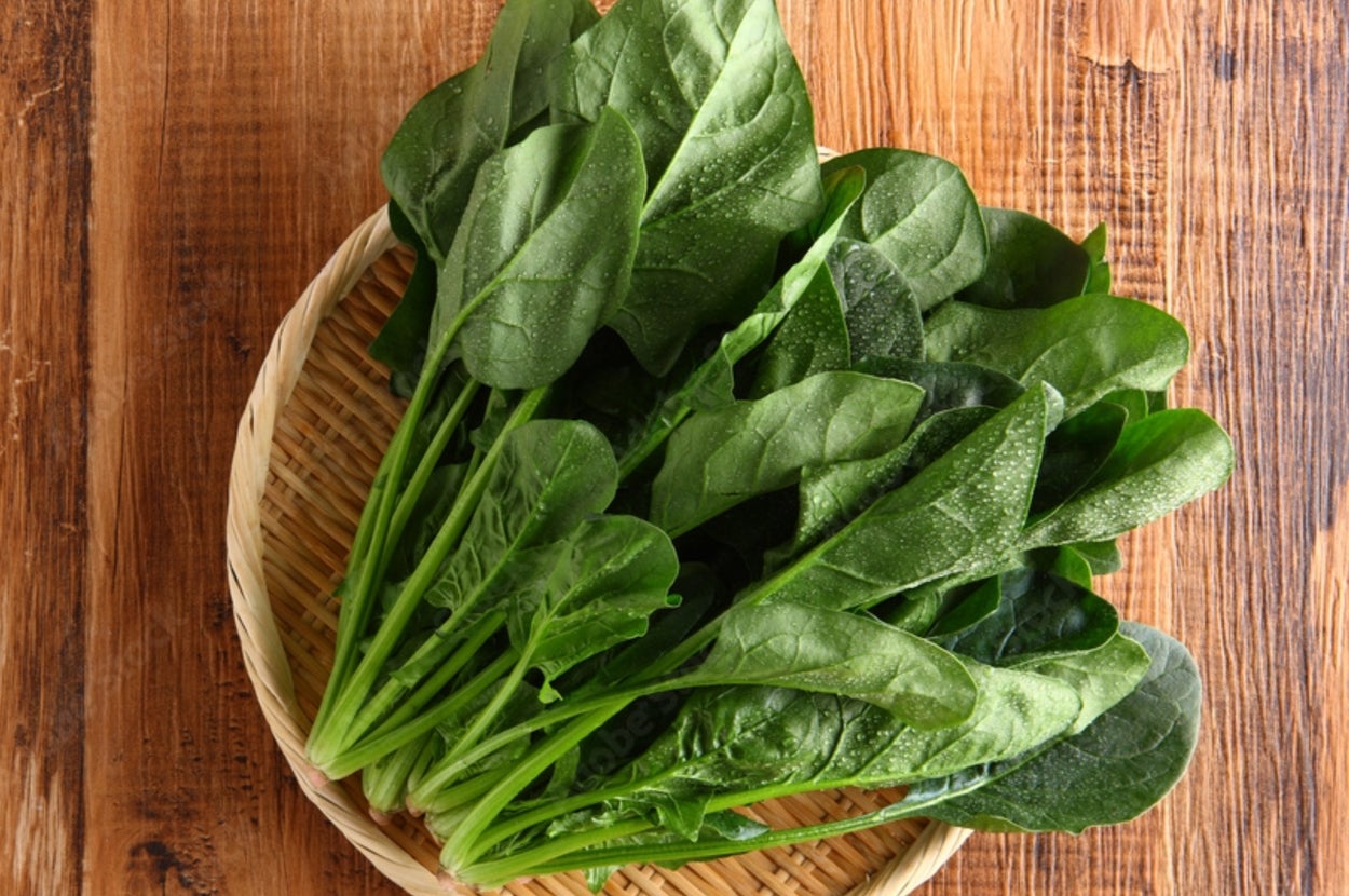 籐の皿にのった新鮮なほうれん草の束が木製テーブルに置かれています。