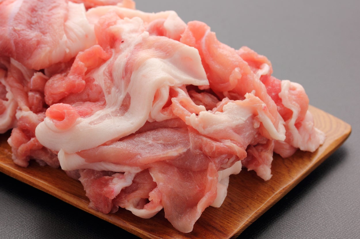 木製のトレイに盛られた生の豚肉のスライス。