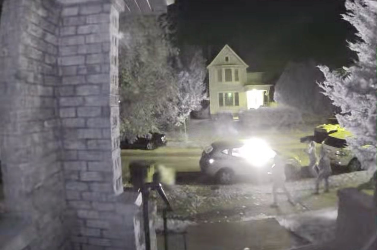 夜の玄関先で車のライトが点灯し、歩行者が通りを歩いている監視カメラ映像。