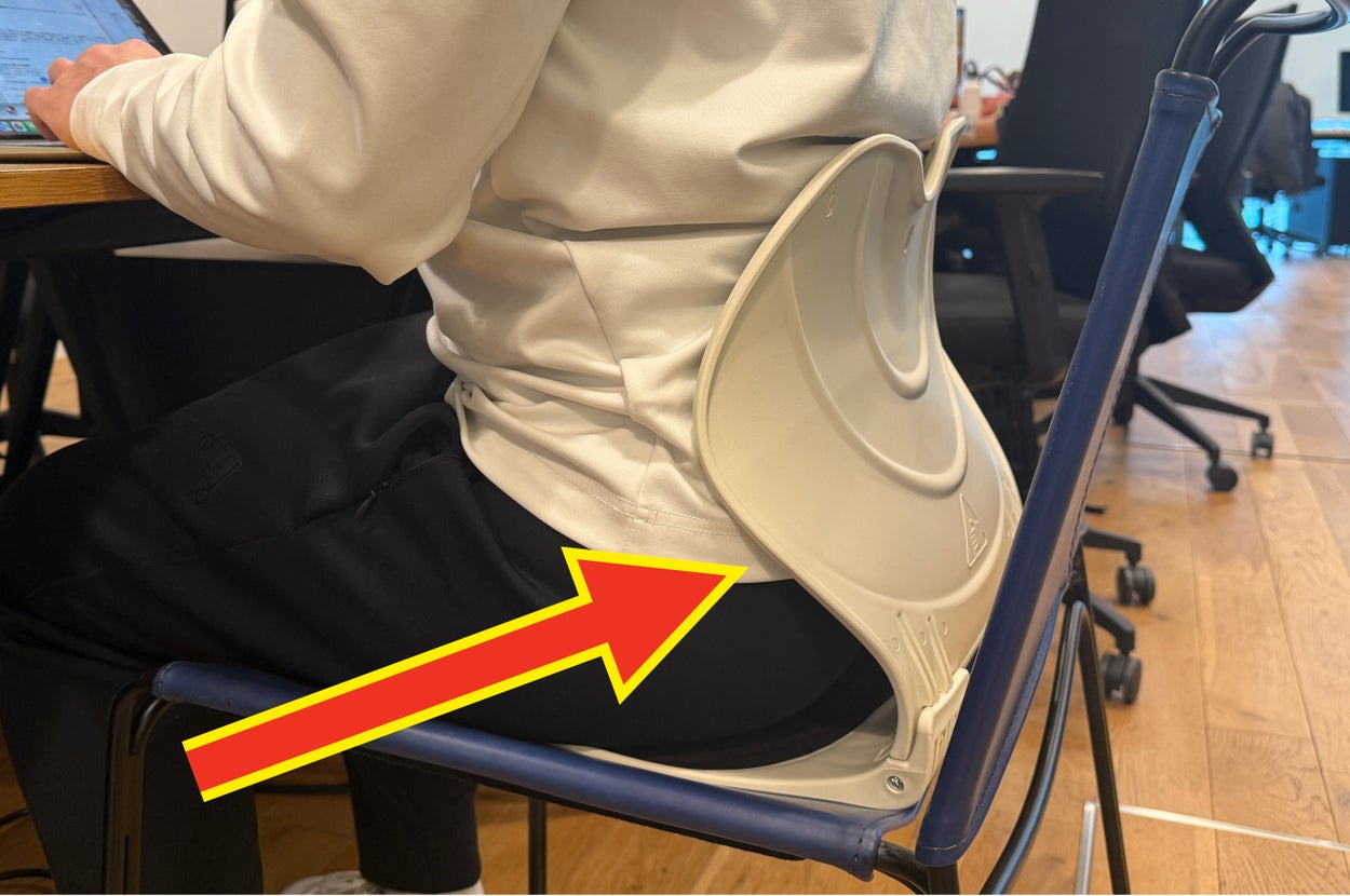 オフィスの机でノートパソコンを使い、サポートクッションを椅子に付けて座っている人。