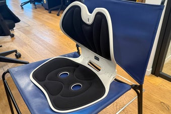 オフィスの椅子に腰サポートを取り付けて座っている人。姿勢補助具を使用中。