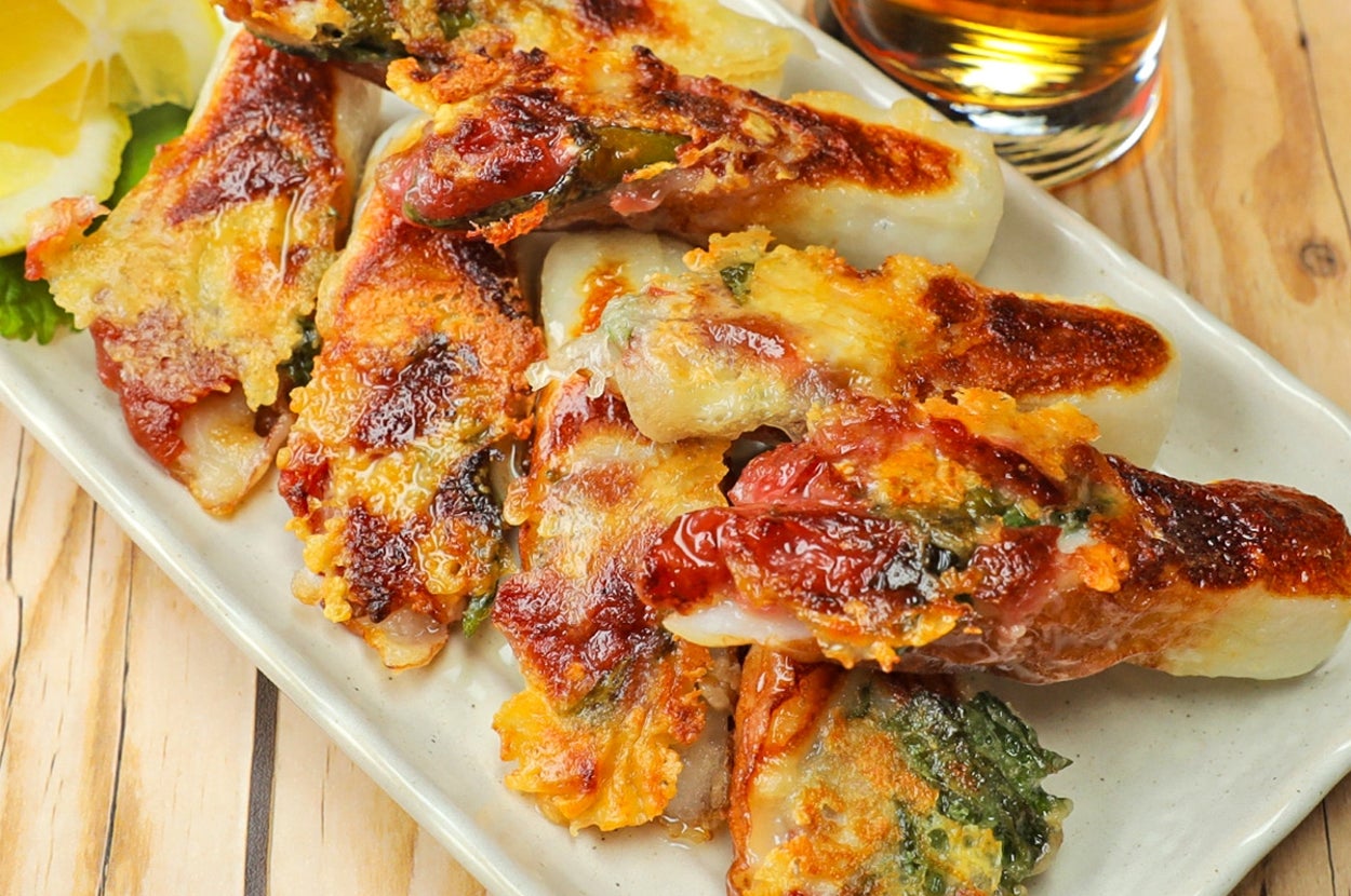 焼き餃子が皿に盛られ、隣にはレモンのくし切りとグラスがあります。